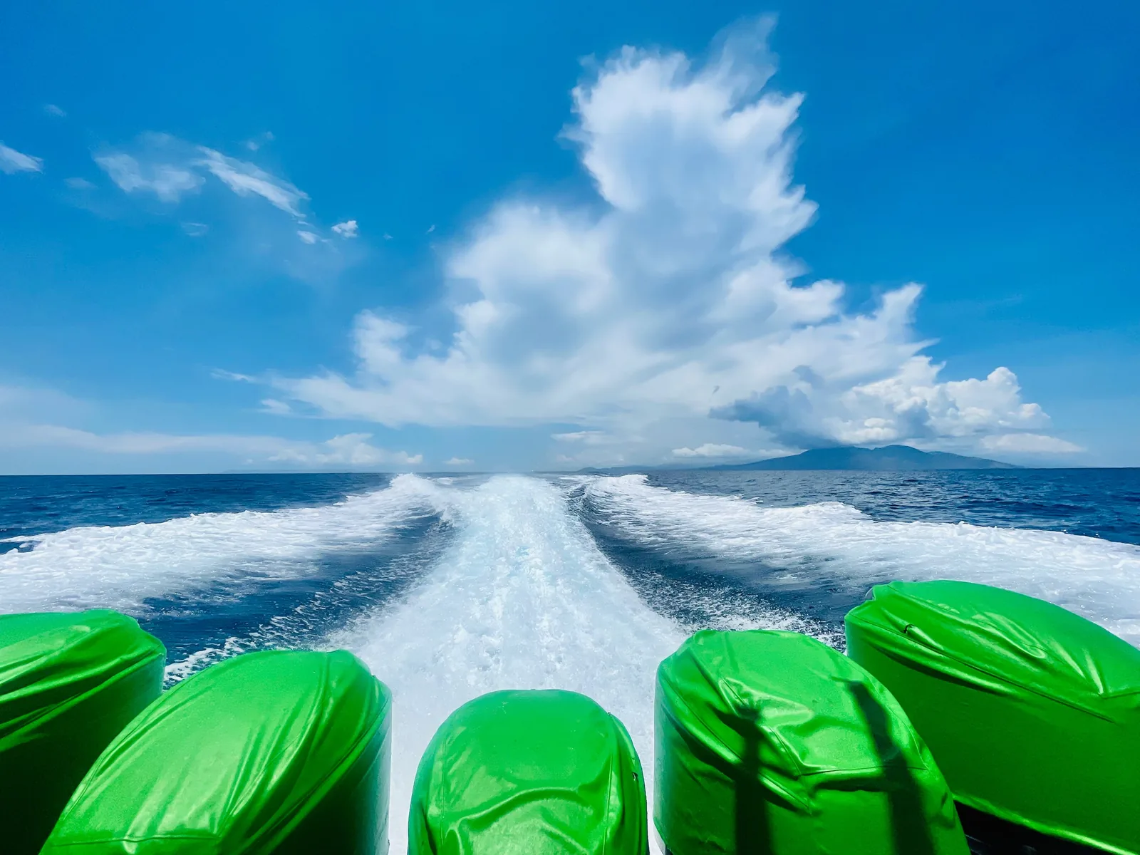 The waves from a ferry boat with Green engine covers and a blue sky