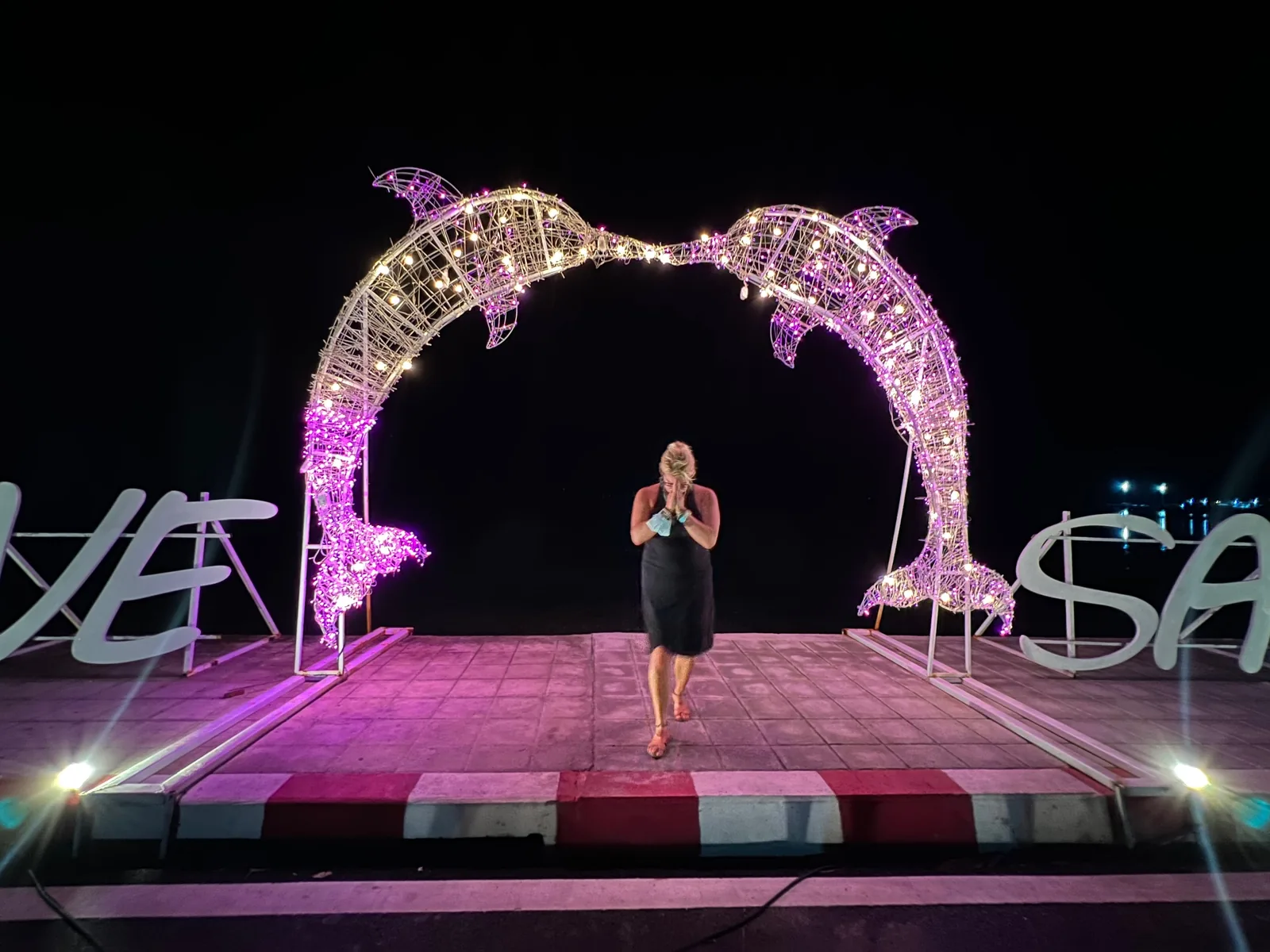 A woman standing in prayer pose under two lit up dolphins