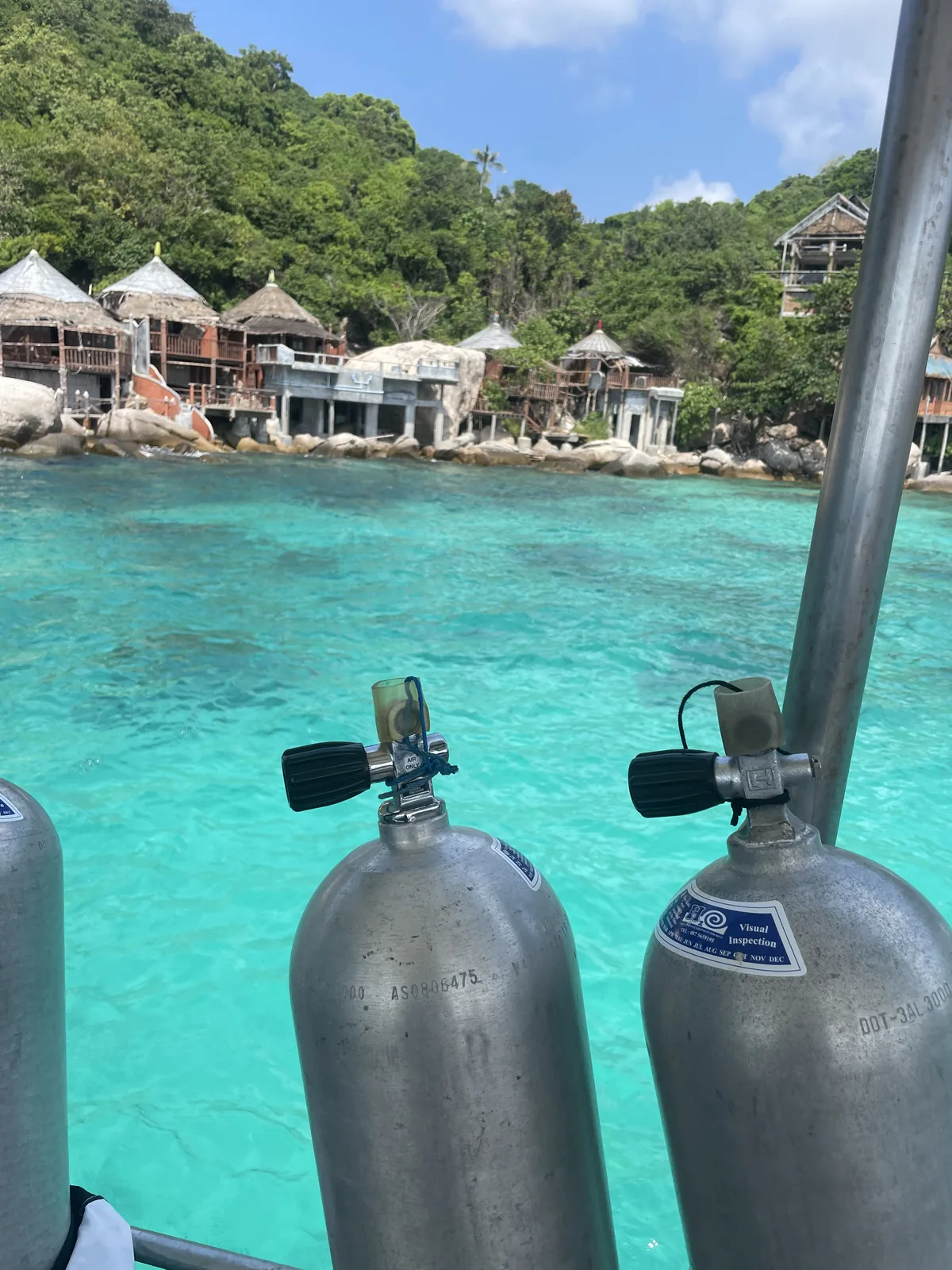 Scuba Diving tanks on a boar with blue Sea and wooden bungalows in the background