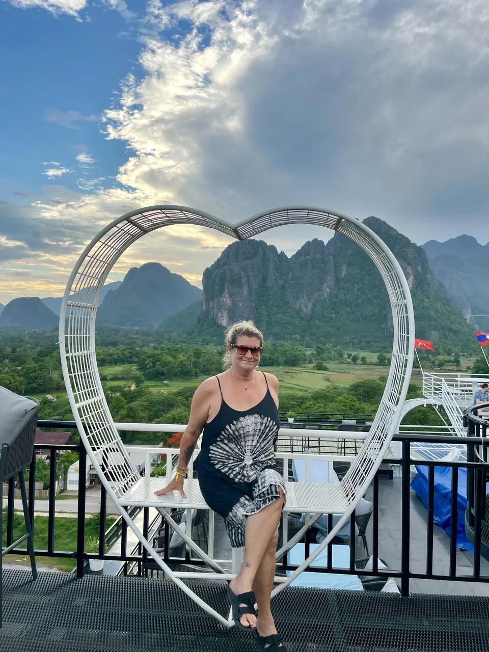 Jennifer at a rooftop bar in Vang Vieng with the karst mountains and a Lao flag at sunset