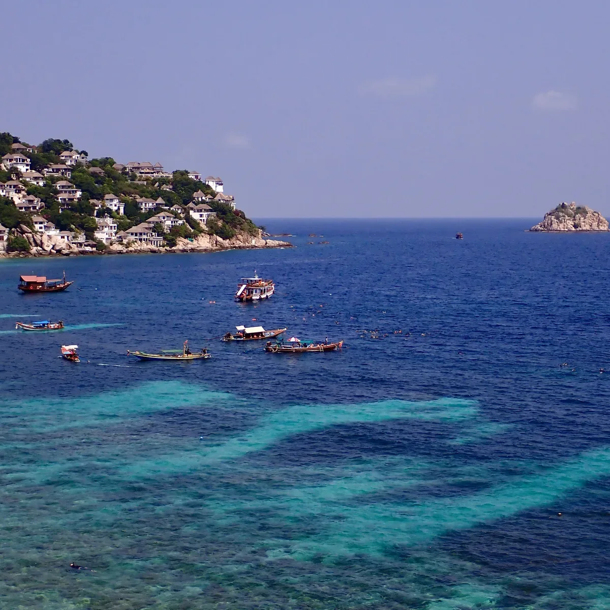 Shark Bay on Koh Tao, long-tail and dive boats moored over the turquoise reef, the hill houses behind